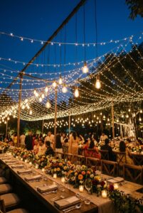 Warm Edison string lights strung in canopy style above outdoor wedding reception tables at twilight — portrait orientation
