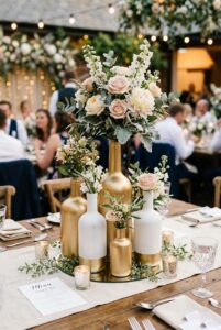 Gold and matte white spray-painted glass vases of varying heights grouped on a wedding table — portrait orientation