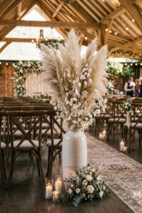 Tall vase with dried pampas grass and dried lunaria stems used as wedding aisle decor in a boho ceremony space — portrait orientation