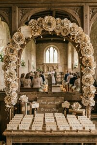 Handcrafted paper roses made from vintage book pages displayed on a wedding arch and escort card table — portrait 2:3