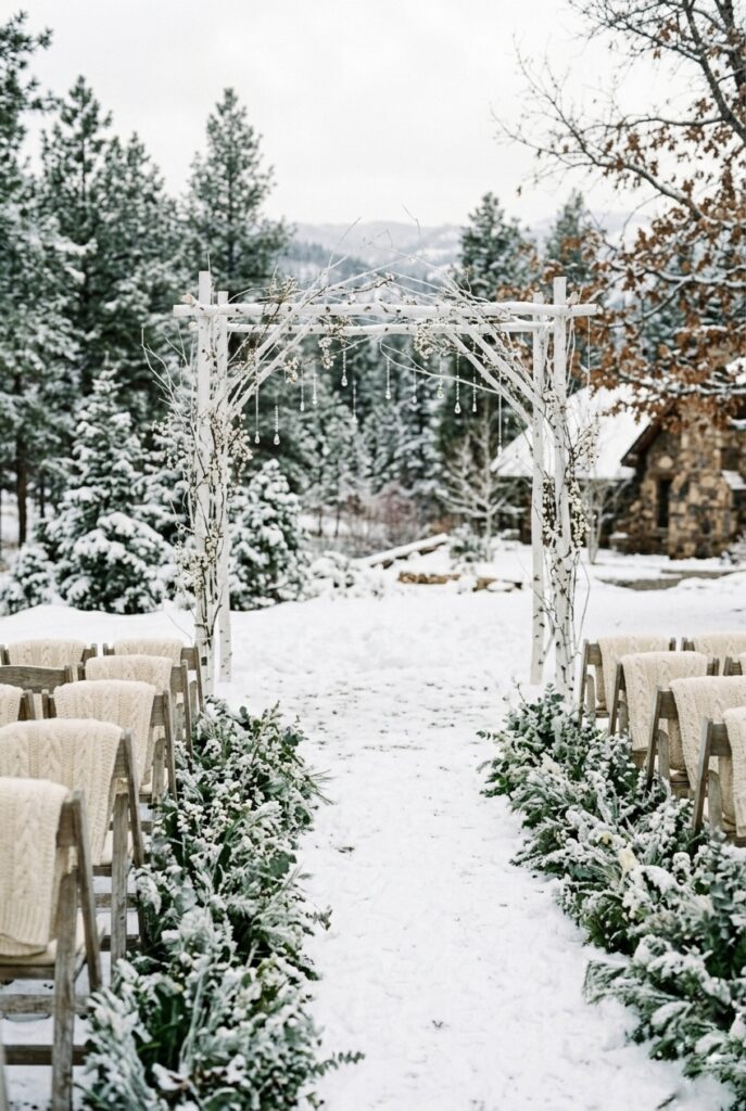 Minimalist winter wedding ceremony arch made from bare frosted white branches, with small hanging crystal ornaments and sprigs of white berries