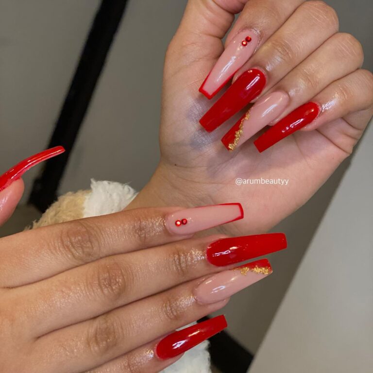 Alt text: Red gel nails with applied gold foil patches, bridal nail art, warm luxurious nail detail, ring shot