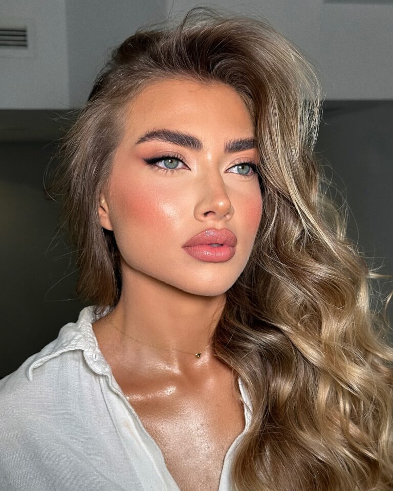Alt text: Bride with soft coral cream blush on cheeks and matching coral lip tint, warm luminous bridal makeup, summer outdoor ceremony