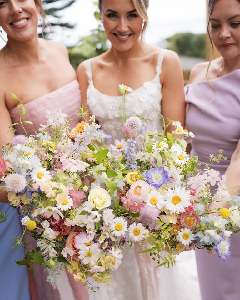 Alt text: Bride holding a loose wildflower bouquet with mixed seasonal stems, natural outdoor wedding style